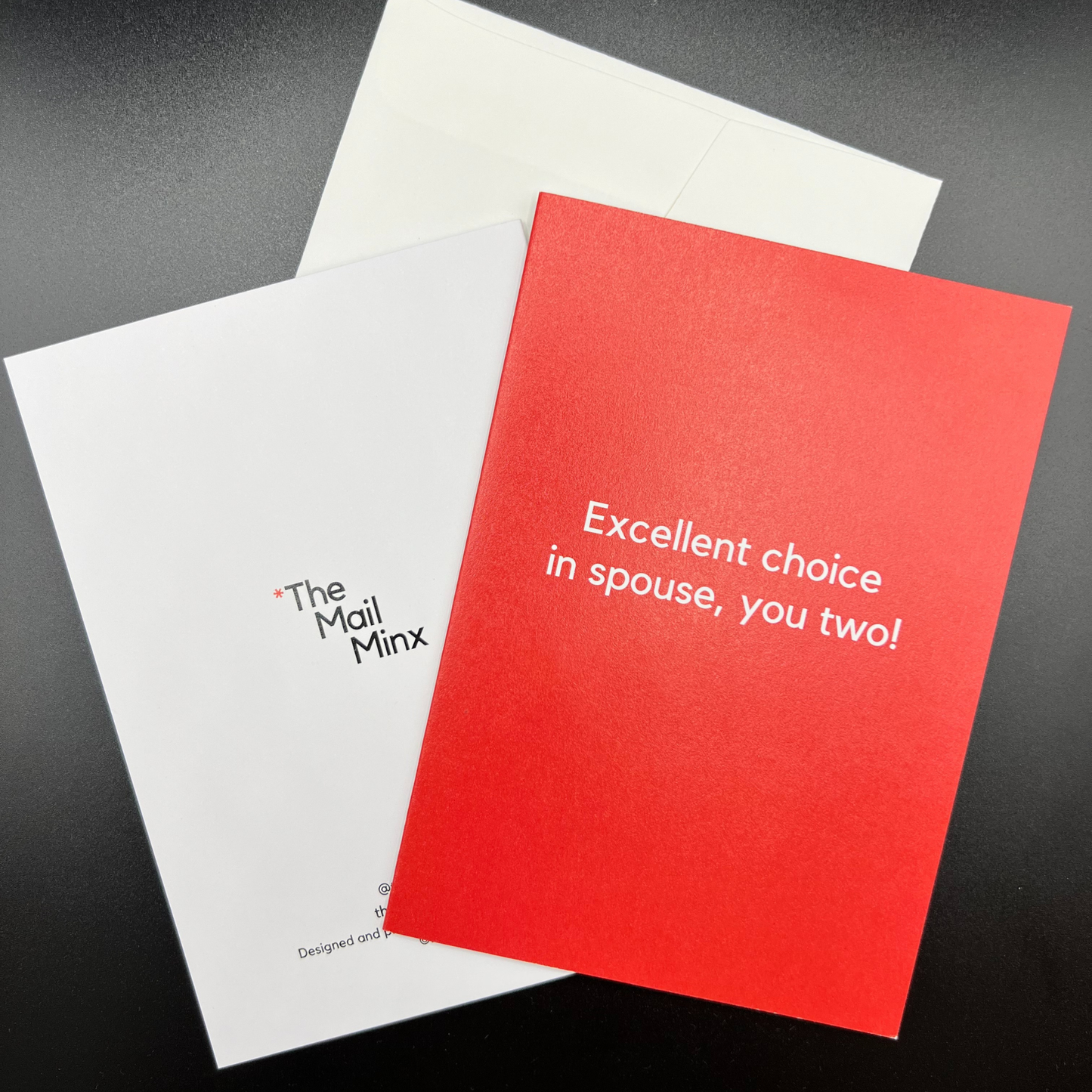 A wedding greeting card by The Mail Minx that is red, with text in white saying "Excellent choice in spouse, you two!" with a white envelope, and another card showing the back that has a logo.