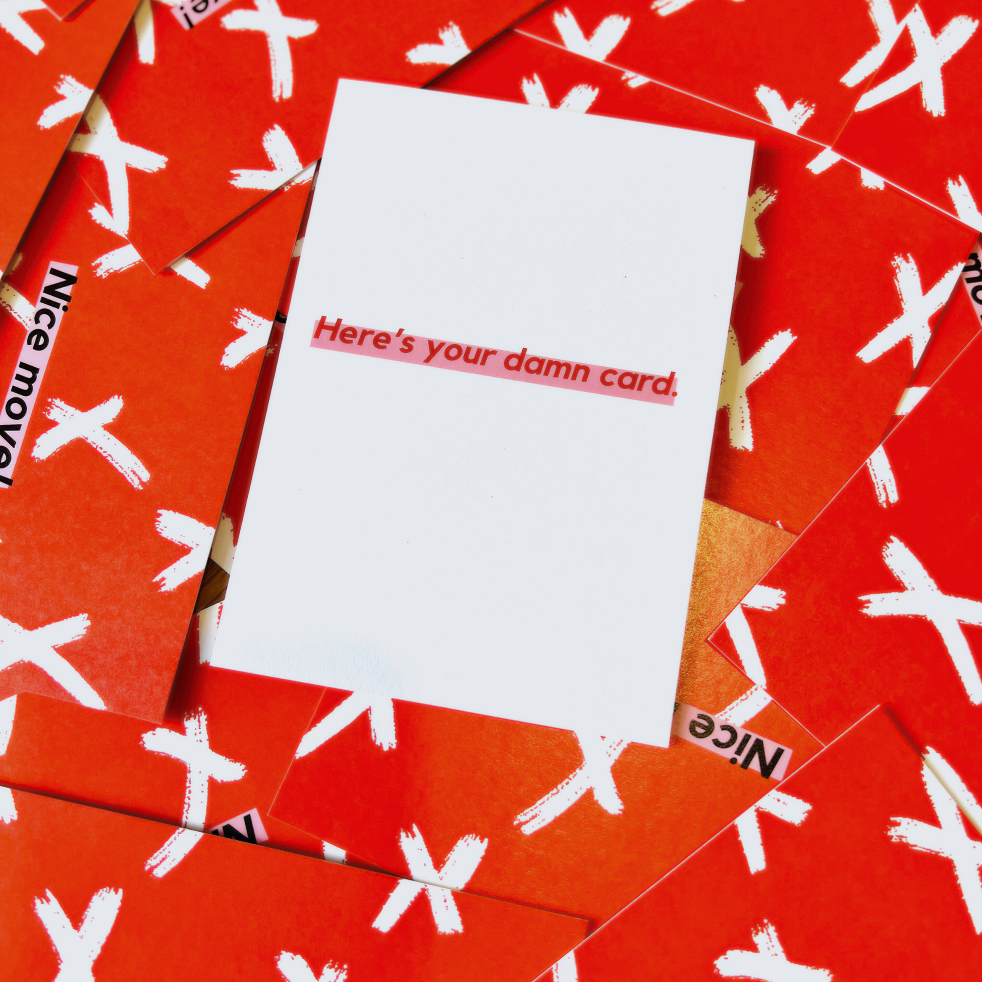 A white greeting card by The Mail Minx with the caption "Here's your damn card" in red text highlighted in pink - card is placed on a red background