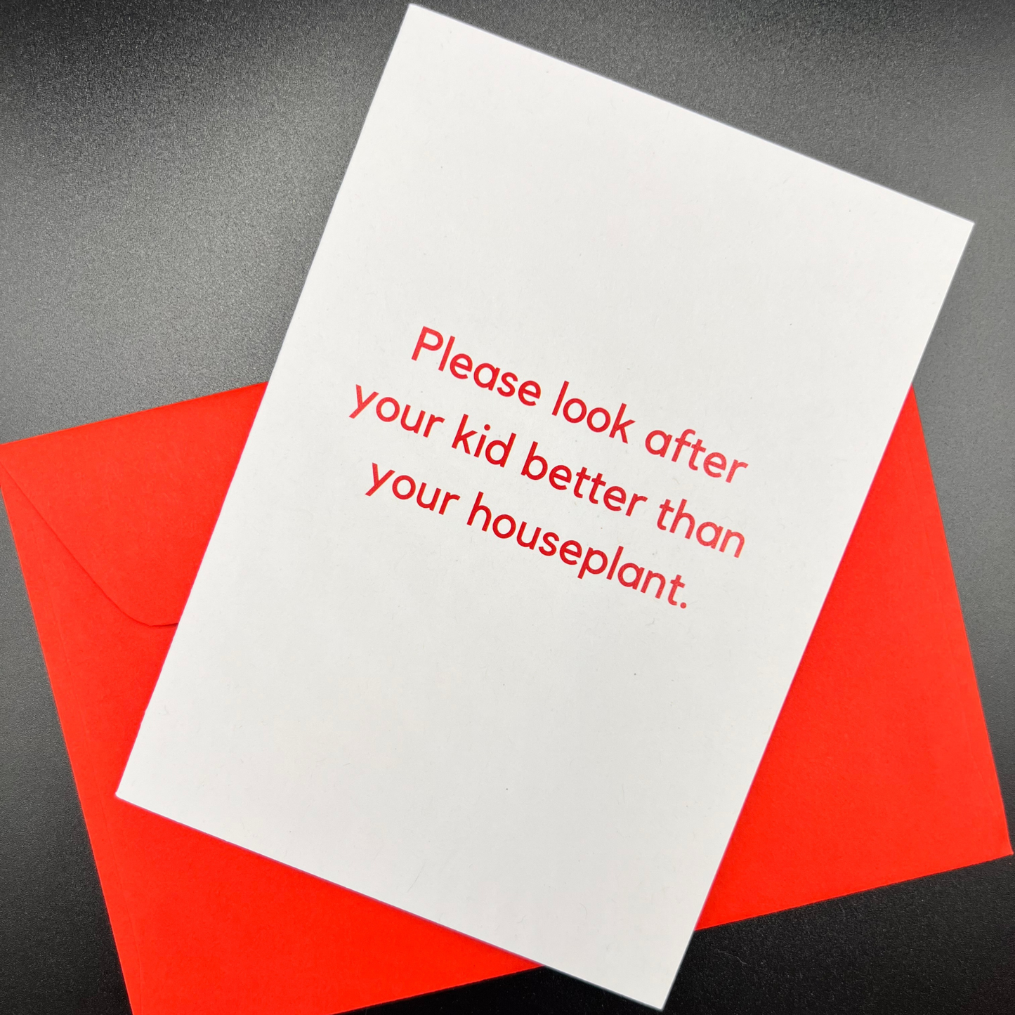 The Mail Minx funny baby shower greeting card that is white and says "Please look after your kid better than your houseplant" in red; with a red envelope
