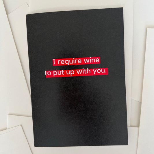 A funny greeting card by The Mail Minx that is black and has a message in white text that says "I require wine to put up with you" that is highlighted in red.