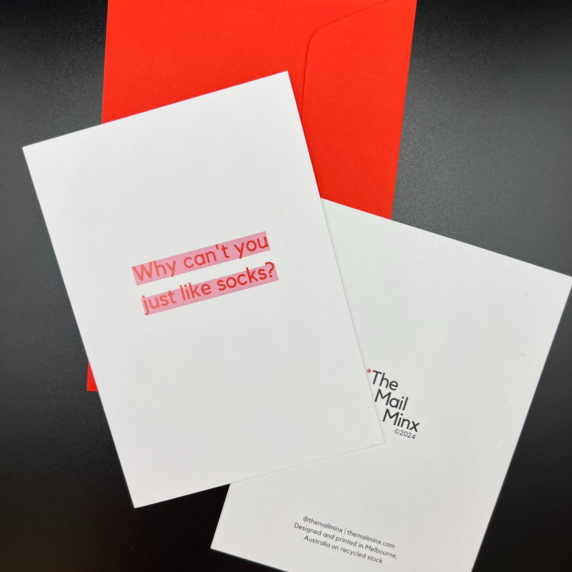A red envelope and the front and back of a funny greeting card by The Mail Minx that says "Why can't you just like socks?" in red text highlighted in pink.