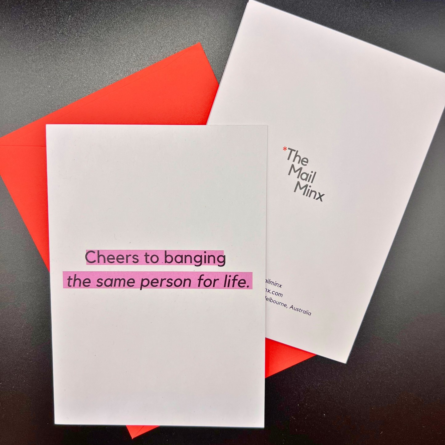 A wedding greeting card by The Mail Minx that says cheers to banging the same person for life in black text highlighted in purple. The card comes with a red envelope, and the back of the card has The Mail Minx logo.