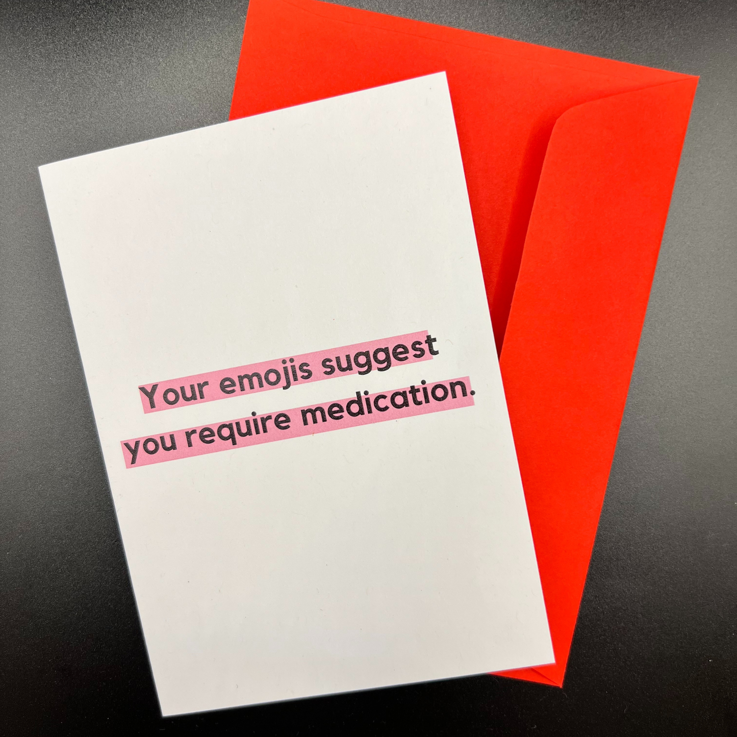 A white funny greeting card that says your emojis suggest you need medication, with a red envelope
