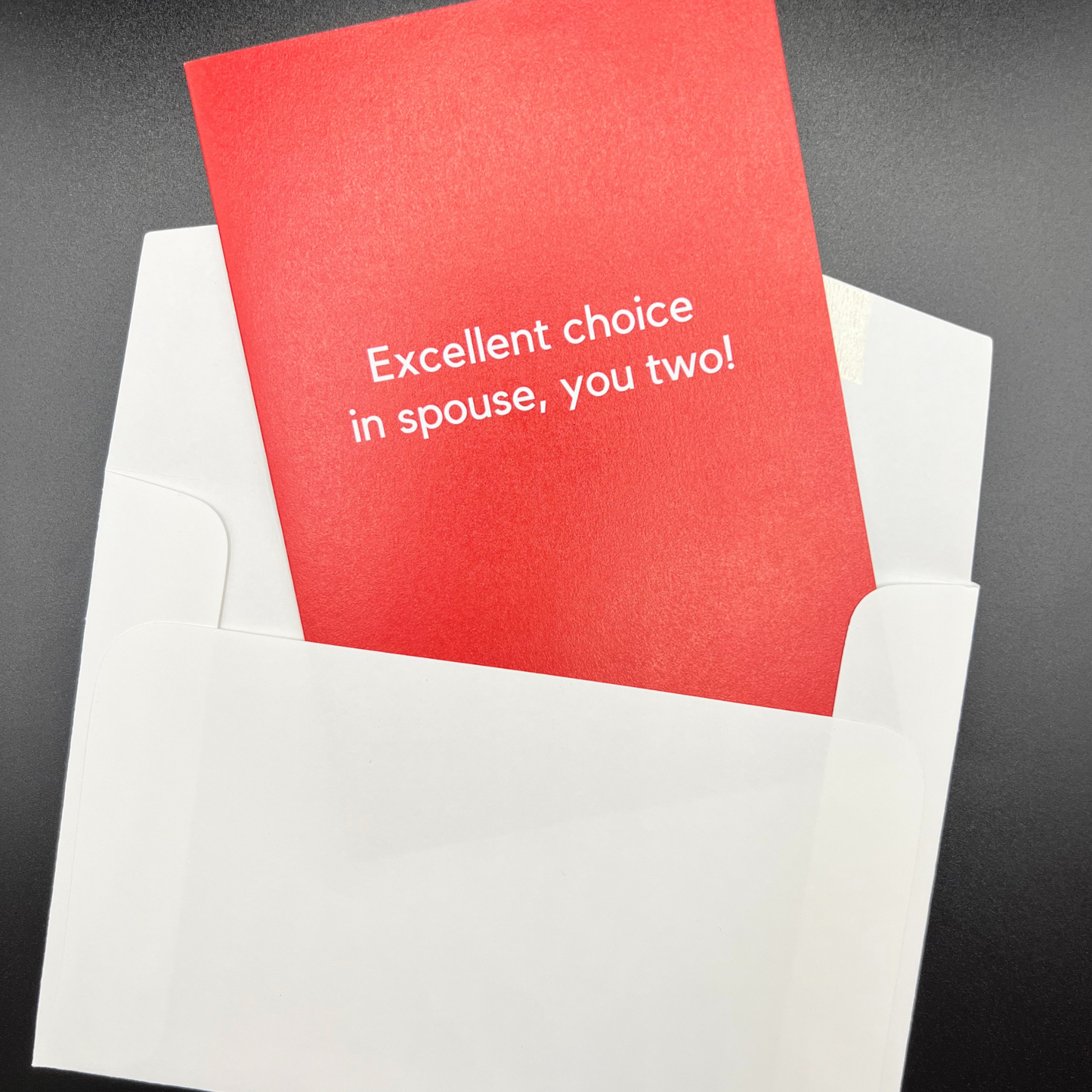 A red wedding greeting card by The Mail Minx with the message in white text "Excellent choice in spouse, you two!" - popping out of a white envelope